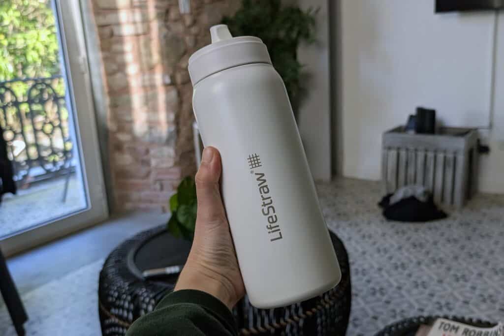 Hand holding a white LifeStraw reusable filtered water bottle inside a bright hotel room in Panama City, promoting sustainable travel and reducing single-use plastic.