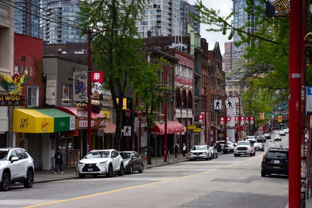 Street view of Vancouver’s Chinatown with shops, red lampposts, and mid-rise buildings along a busy road.