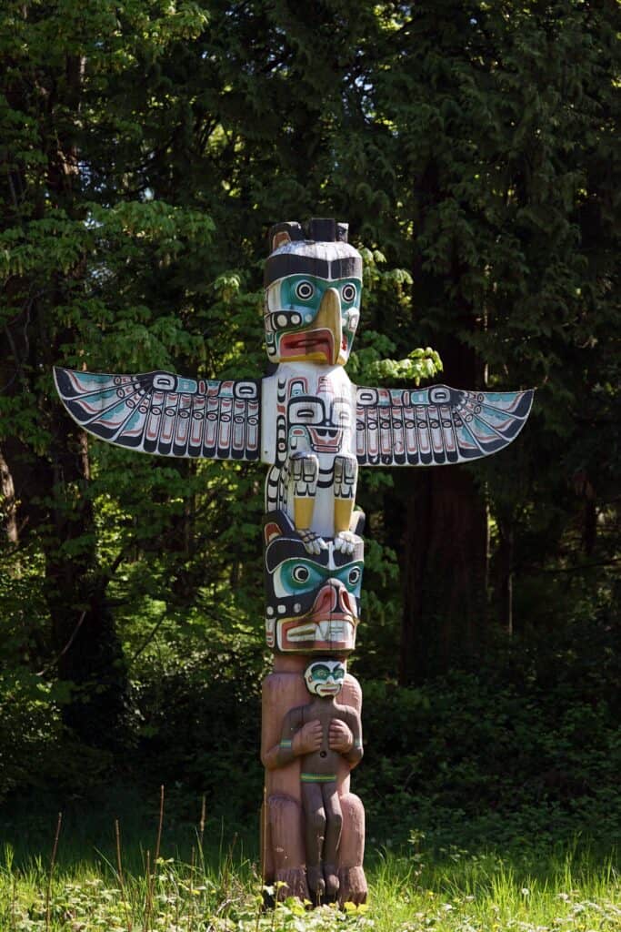 Colorfully painted Indigenous totem pole in Stanley Park surrounded by forest.