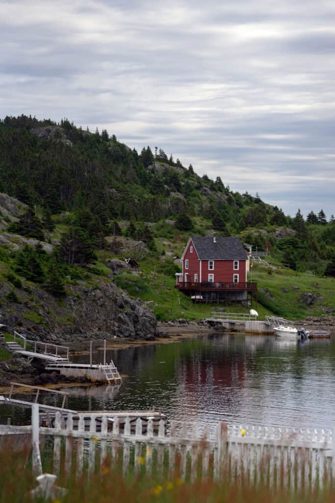 Red saltbox house perched on a rocky hillside above a sheltered cove in the Exploits Islands, Newfoundland and Labrador.