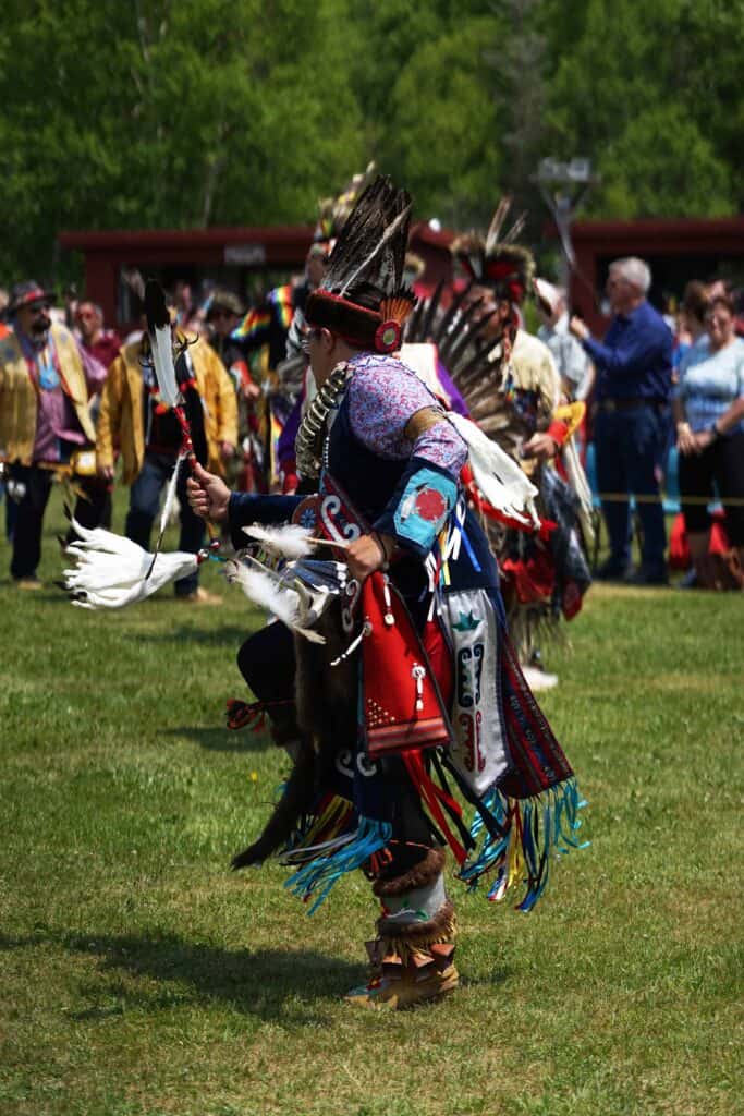 Dancer in regalia performing in the arena during the Miawpukek First Nation Powwow, with tipis and spectators in the background.