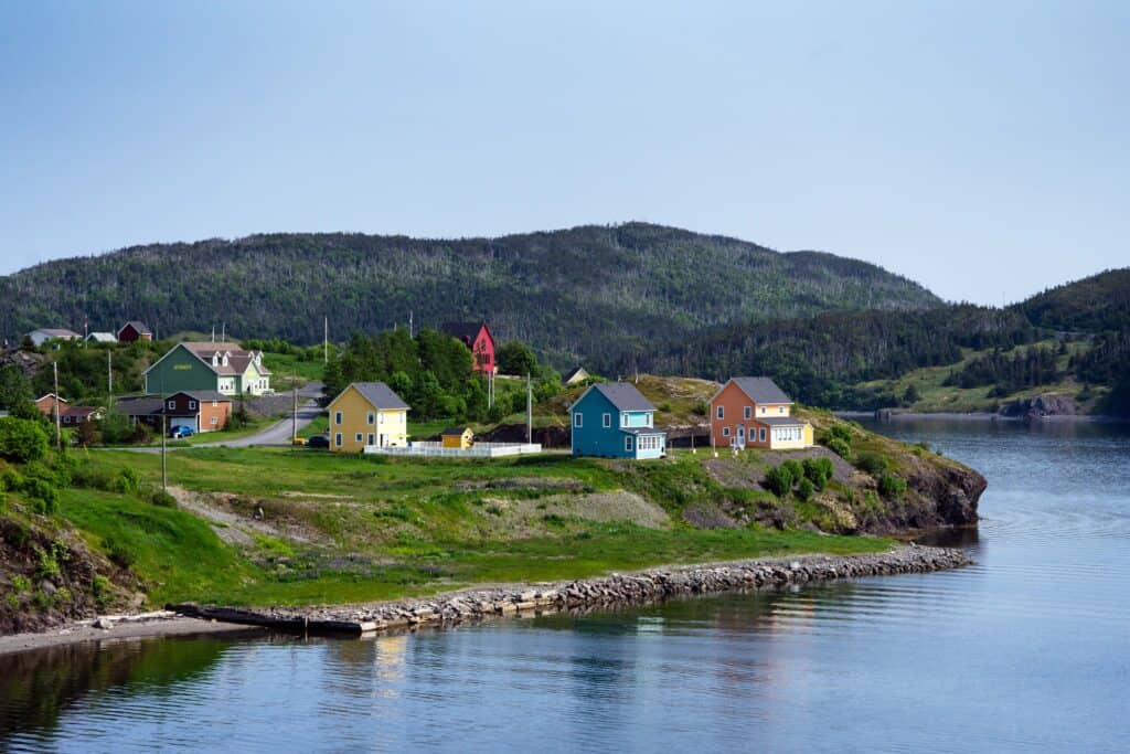 Colourful homes perched along the rocky shoreline in Trinity, Newfoundland and Labrador, with forested hills rising behind the community.