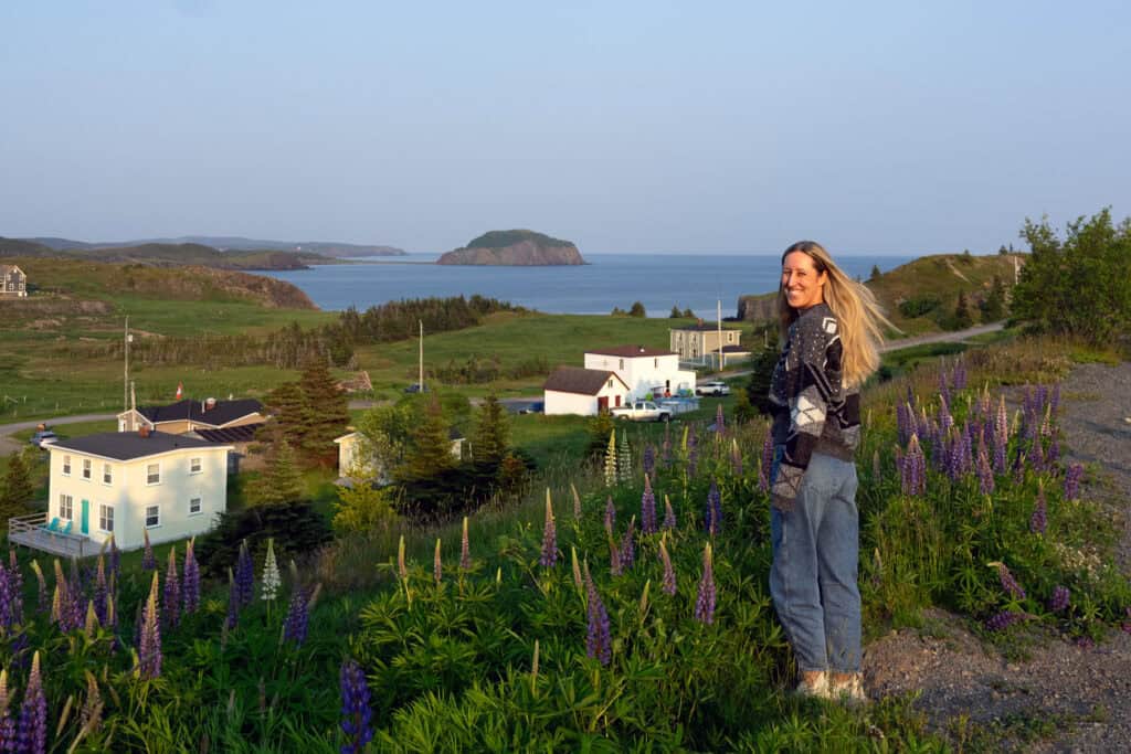 Blonde woman standing with view of coastal Newfoundland and ocean behind her.