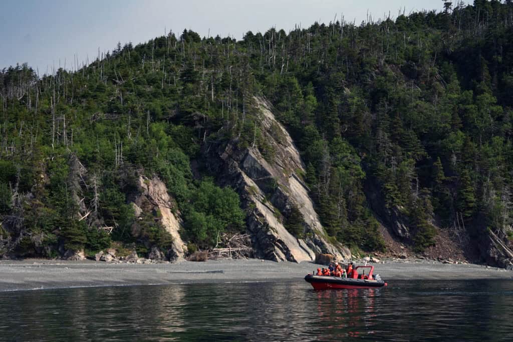 Sea of Whales Adventures Zodiac boat cruising along the coastline near a secluded beach and steep cliffs in Trinity Bay, Newfoundland and Labrador.