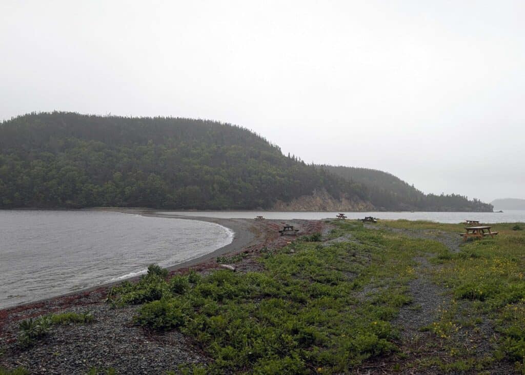 Shoreline and picnic area at The Beaches Archaeological Site in Hare Bay, Newfoundland, with forested hills and coastal views.