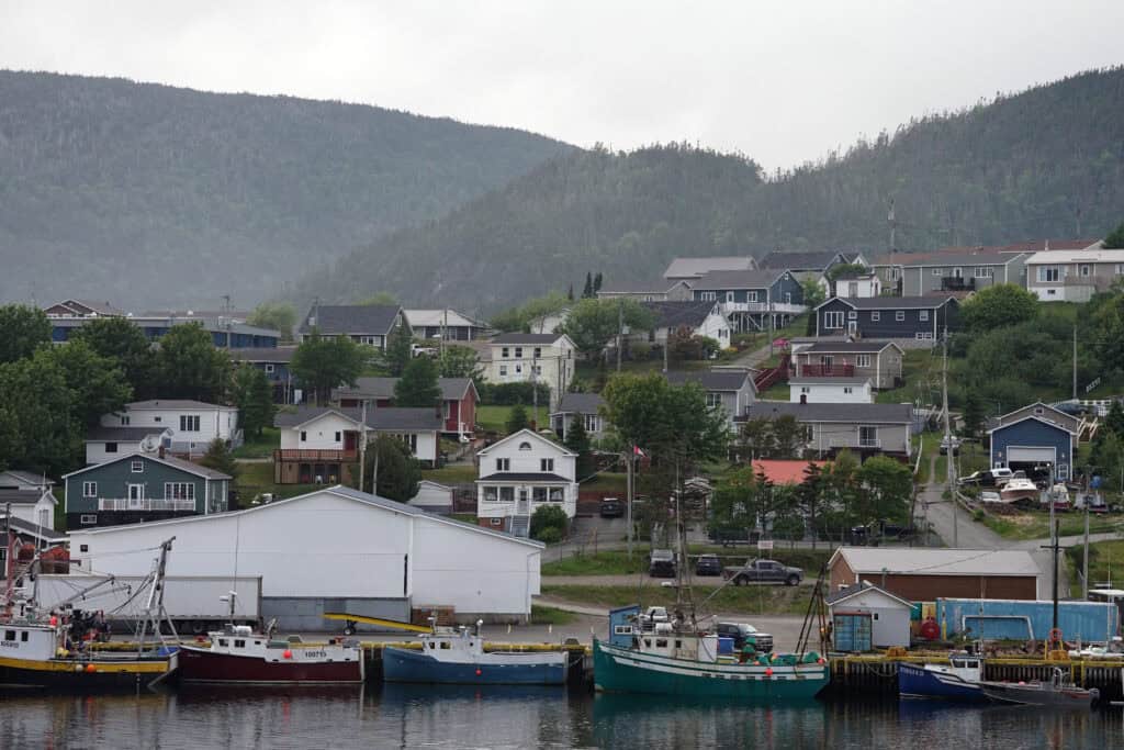 View of Harbour Breton, Newfoundland, with homes overlooking a sheltered harbour backed by steep forested fjords under low cloud.