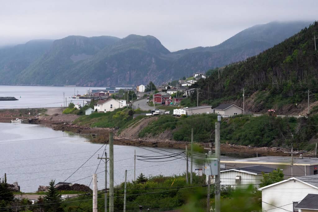 View of Harbour Breton, Newfoundland, with homes overlooking a sheltered harbour backed by steep forested fjords under low cloud.