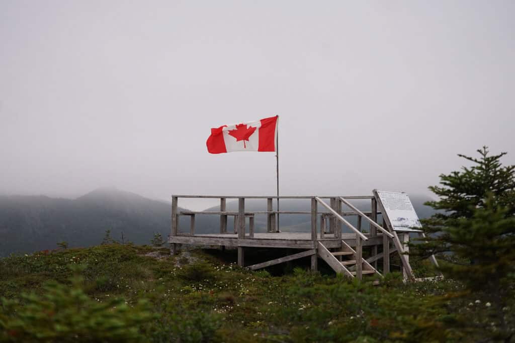 Viewing platform at the summit of Gunn Hill Lookout Trail in Harbour Breton, Newfoundland, with a Canadian flag, interpretive sign, and fog-covered views over the surrounding Coast of Bays hills.