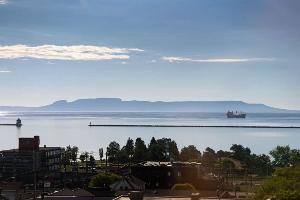 View of the Sleeping Giant across Lake Superior from Thunder Bay, with a cargo ship on the water and buildings in the foreground.
