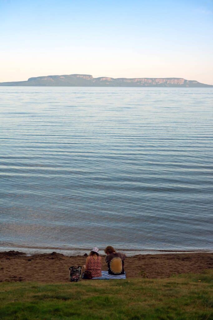 Two people sitting on the shore of Lake Superior with the Sleeping Giant visible across the water in Thunder Bay.