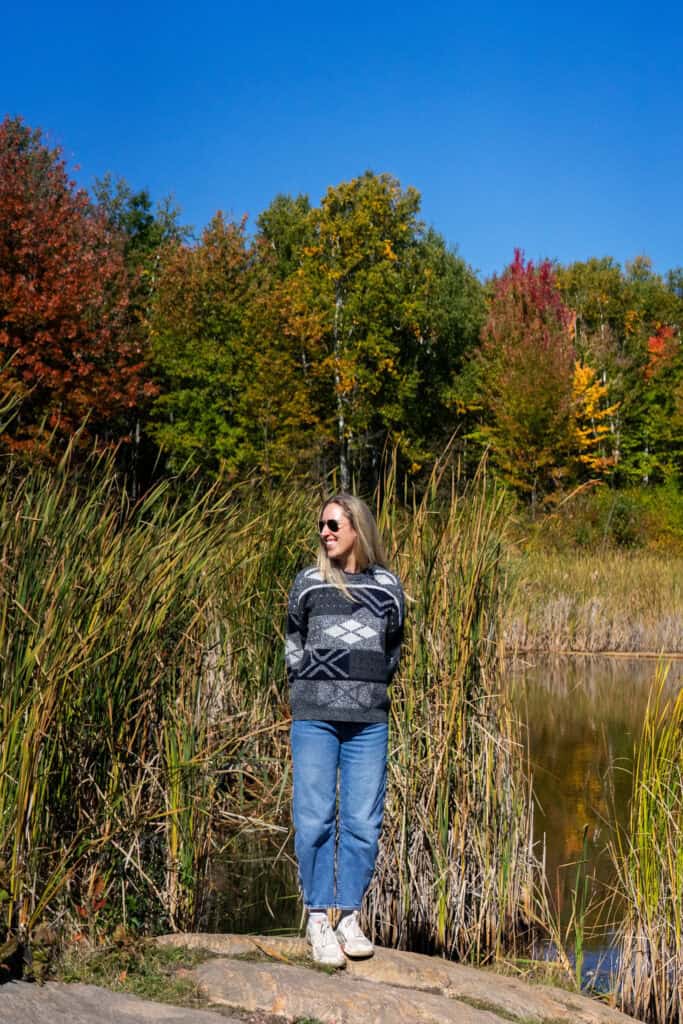 Woman standing beside a wetland surrounded by reeds and colourful fall foliage at Laurier Woods Conservation Area in North Bay, Ontario.