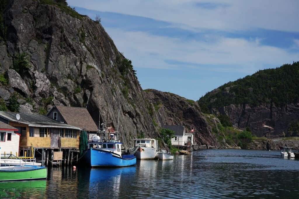 Boats moored beside wooden fishing buildings in Quidi Vidi Harbour, surrounded by steep rocky hills in St. John’s, Newfoundland and Labrador.